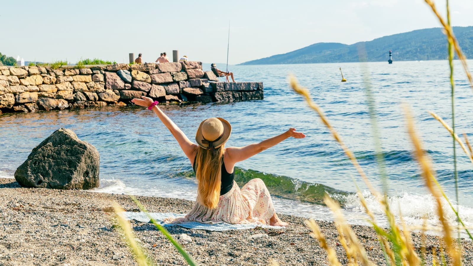 Strandliv i Drøbak og bilde av en dame med henda i været og som sitter på et håndkle