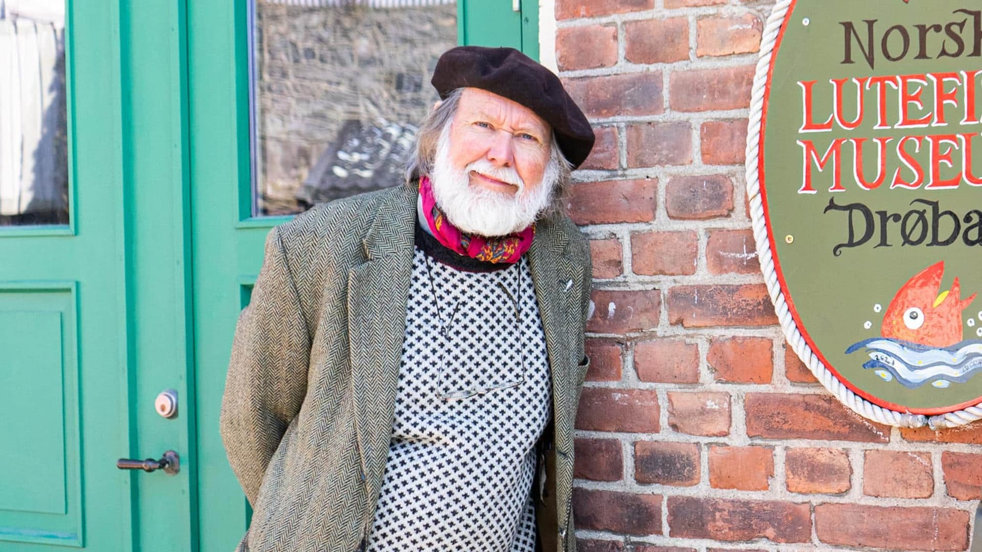 Mann med beret foran et murhus