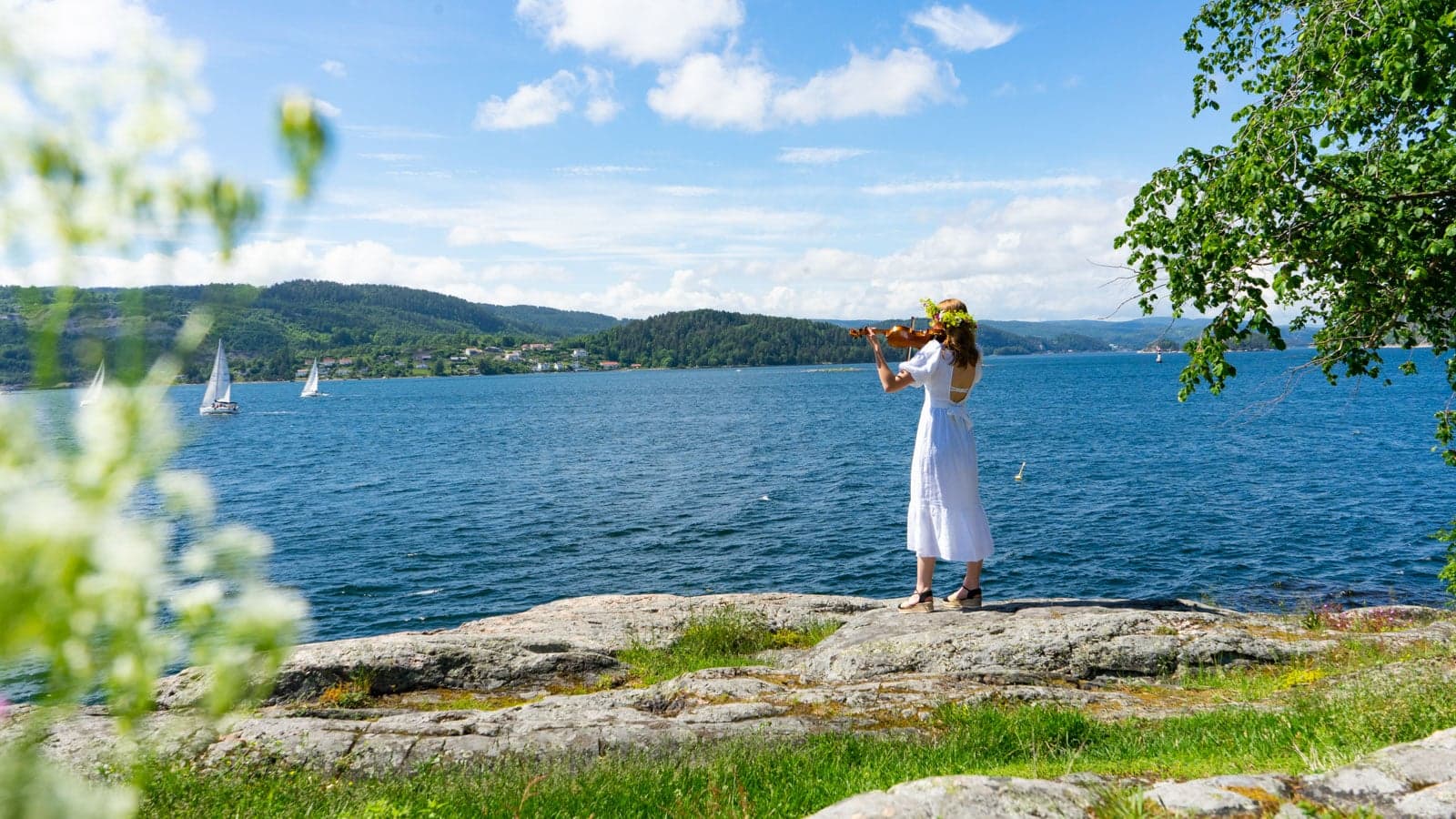 Dame som spiller fiolin med hvit kjole ved fjorden