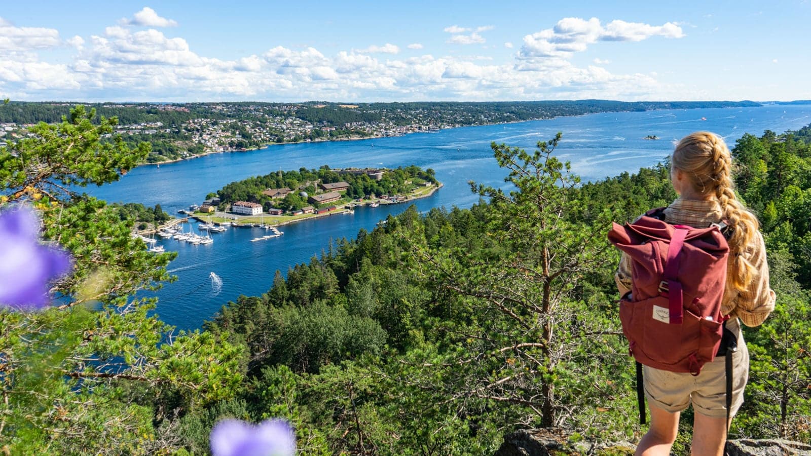 Dame med sekk som ser utover fjorden fra utsikspunkt